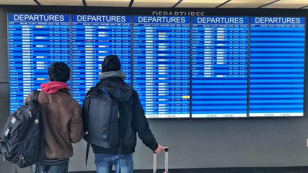 travelers in front of airport departure board